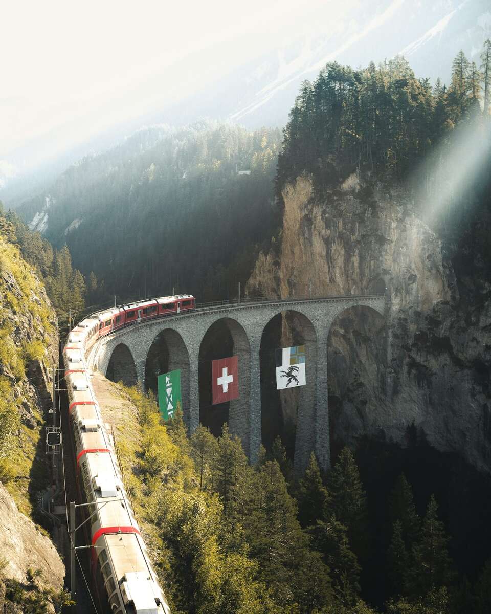 A red train crossing the curved Landwasser Viaduct into a cliff tunnel